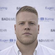 Der Mann hat einen entschlossenen Gesichtsausdruck und steht vor einem Hintergrund mit dem Schriftzug 'BAD & MEHR'.